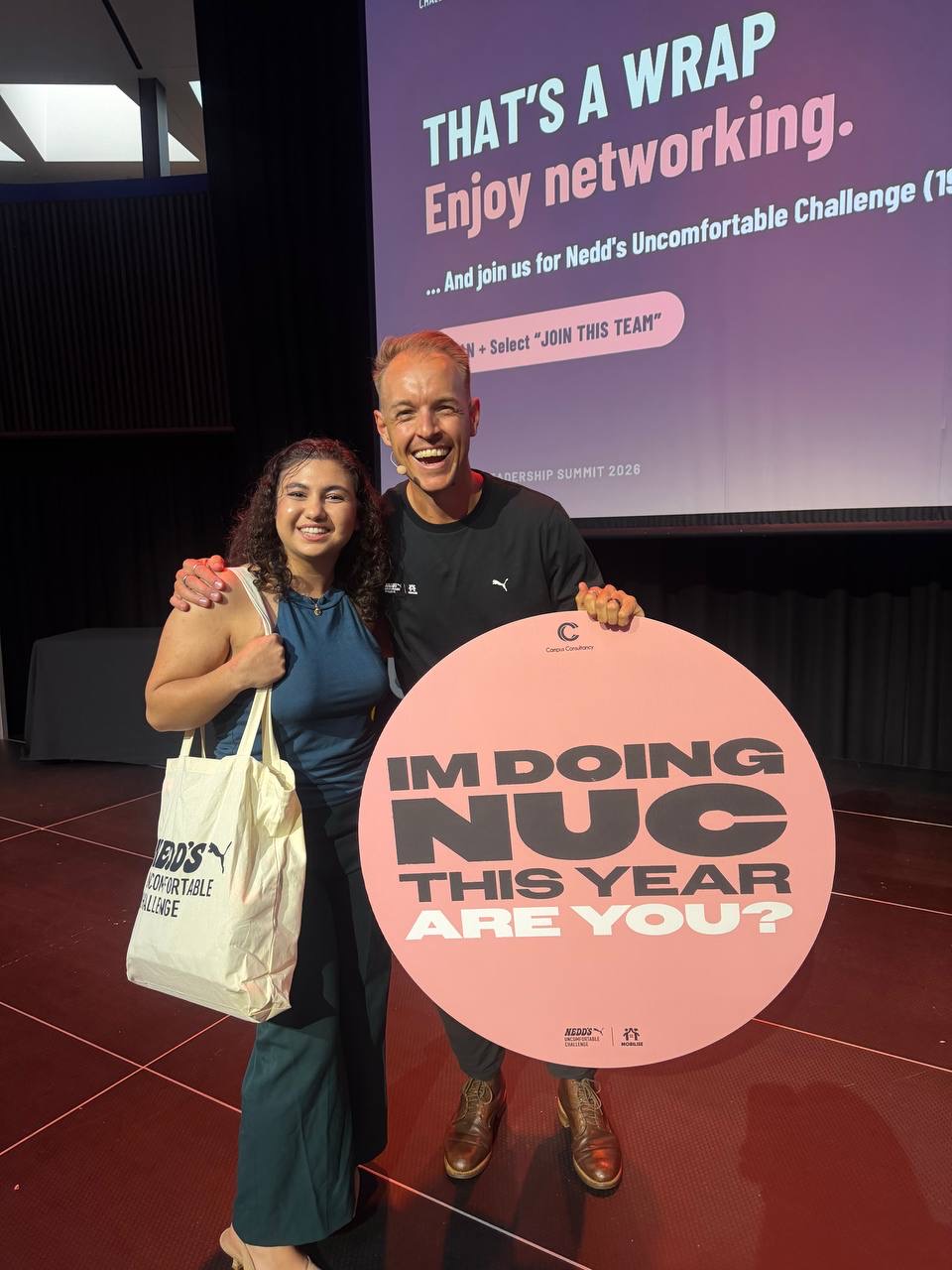 Rodmina at the summit beside a participant holding a Nedd’s Uncomfortable Challenge sign